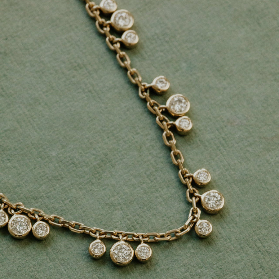 Gold necklace with diamond pendants on a green background