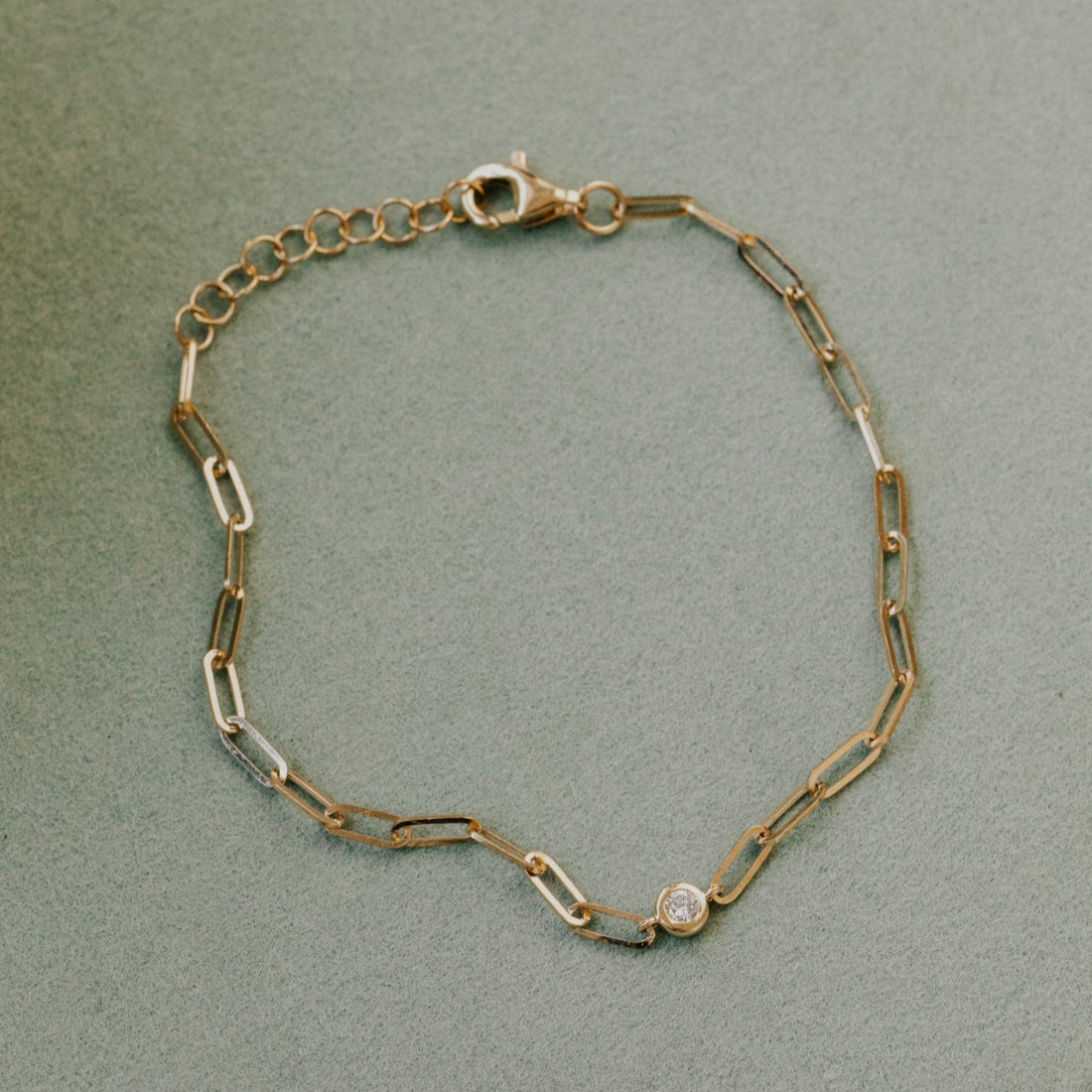 Gold chain bracelet with a diamond on a light green background