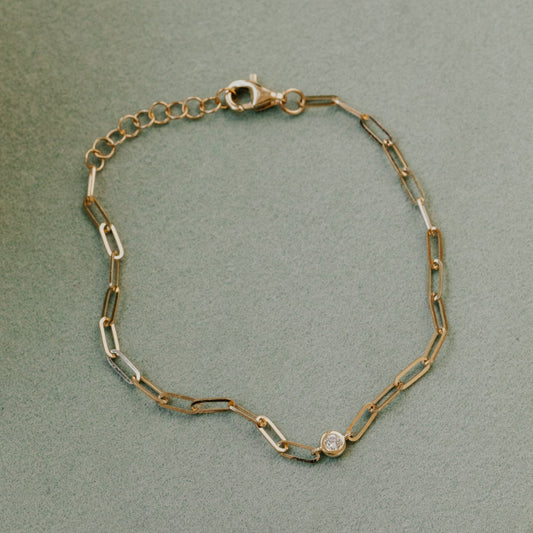 Gold chain bracelet with a diamond on a light green background