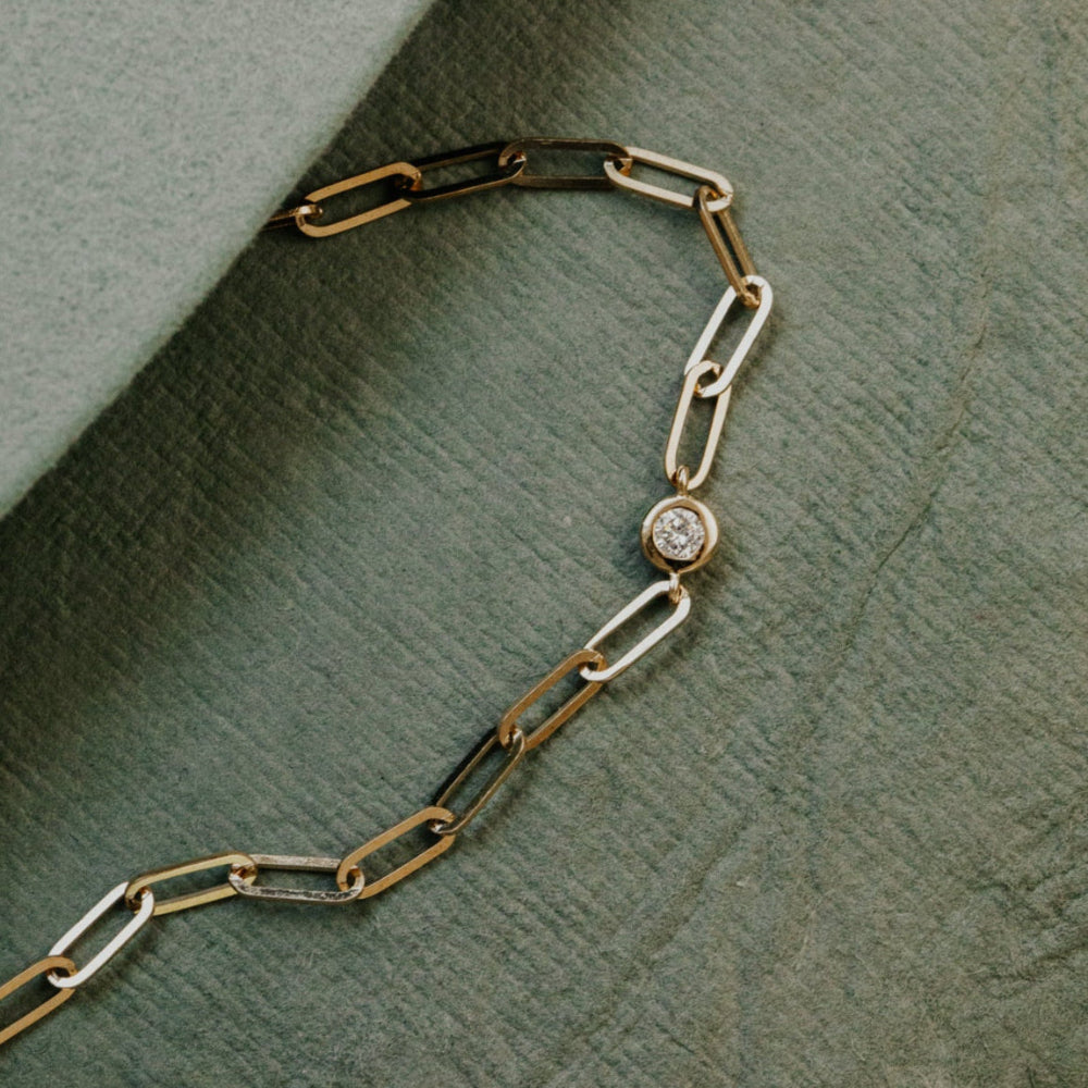 Gold chain bracelet with a diamond pendant on a textured green surface