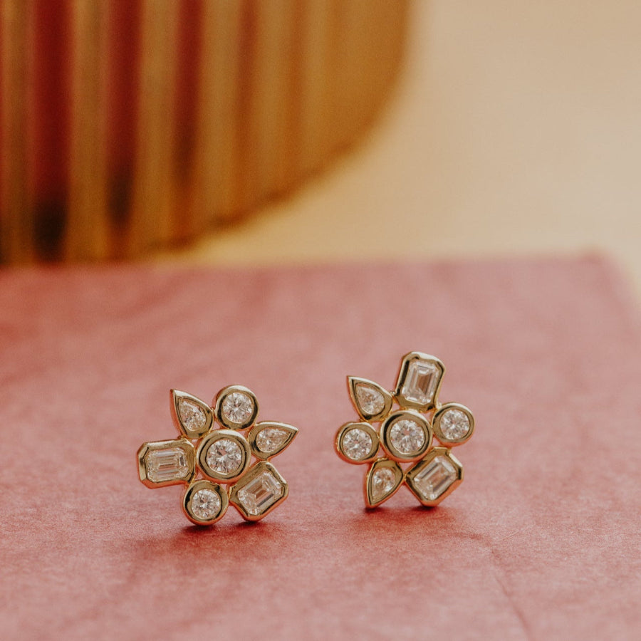 Pair of gold earrings with diamond accents on a pink surface