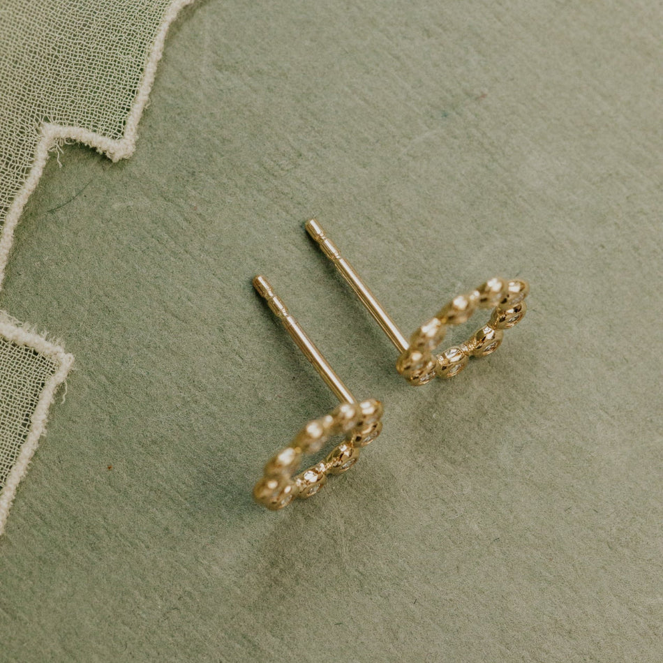 Gold earrings with pearl-like beads on a green fabric background