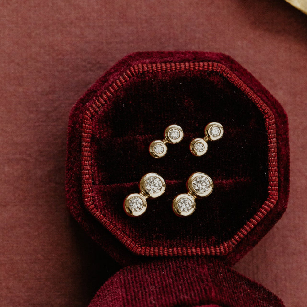Set of diamond stud earrings in a burgundy velvet box on a matching background