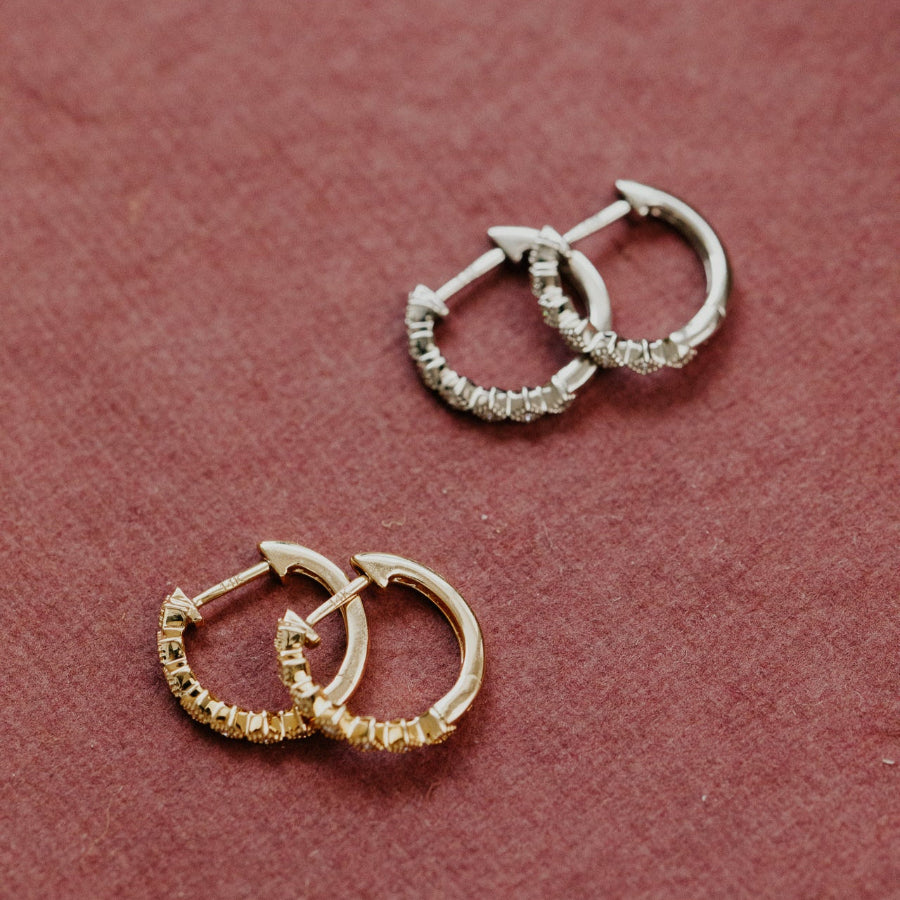 Two pairs of hoop earrings, one yellow gold and one white gold on a pink background.