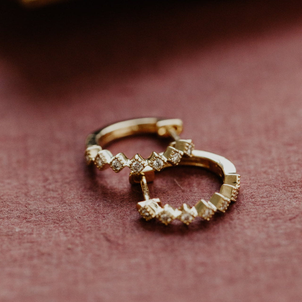 Gold hoop earrings with diamond-like stones on a pink background