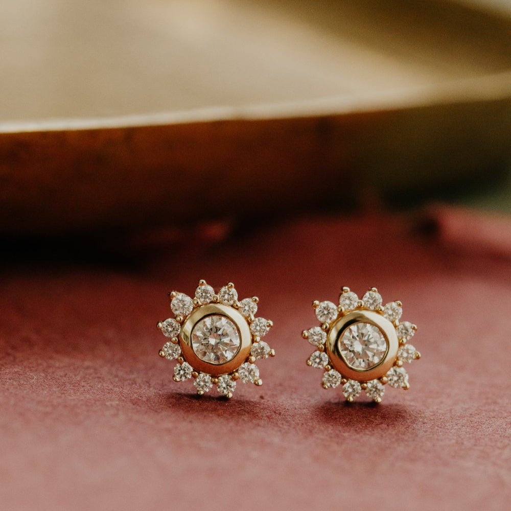 Pair of gold earrings with diamond accents on a soft pink background