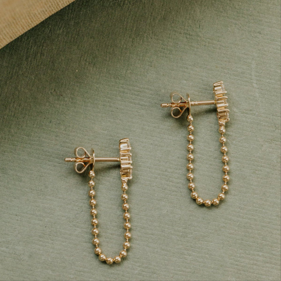 Pair of gold chain earrings on a green surface