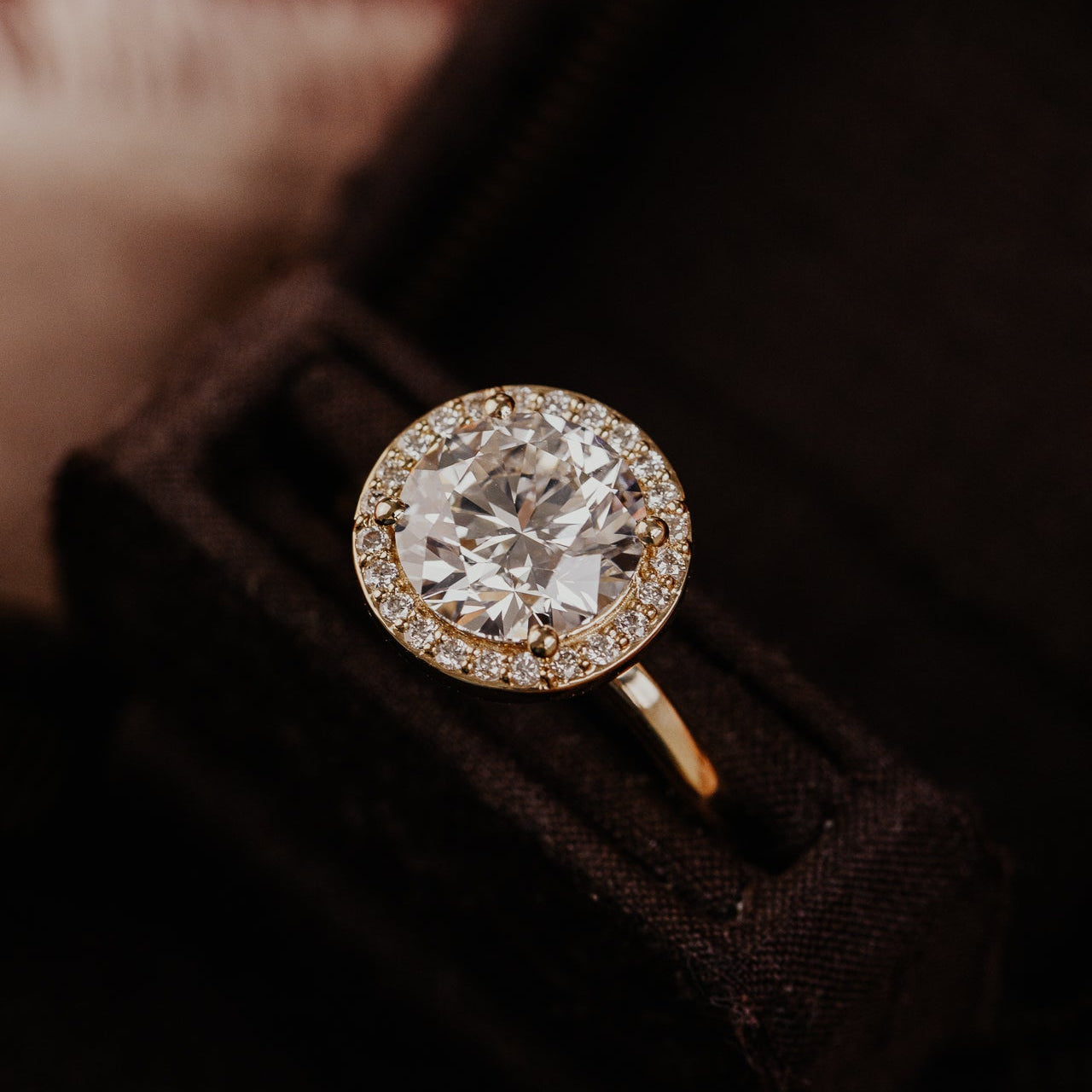 Round diamond ring with gold band on a dark fabric background