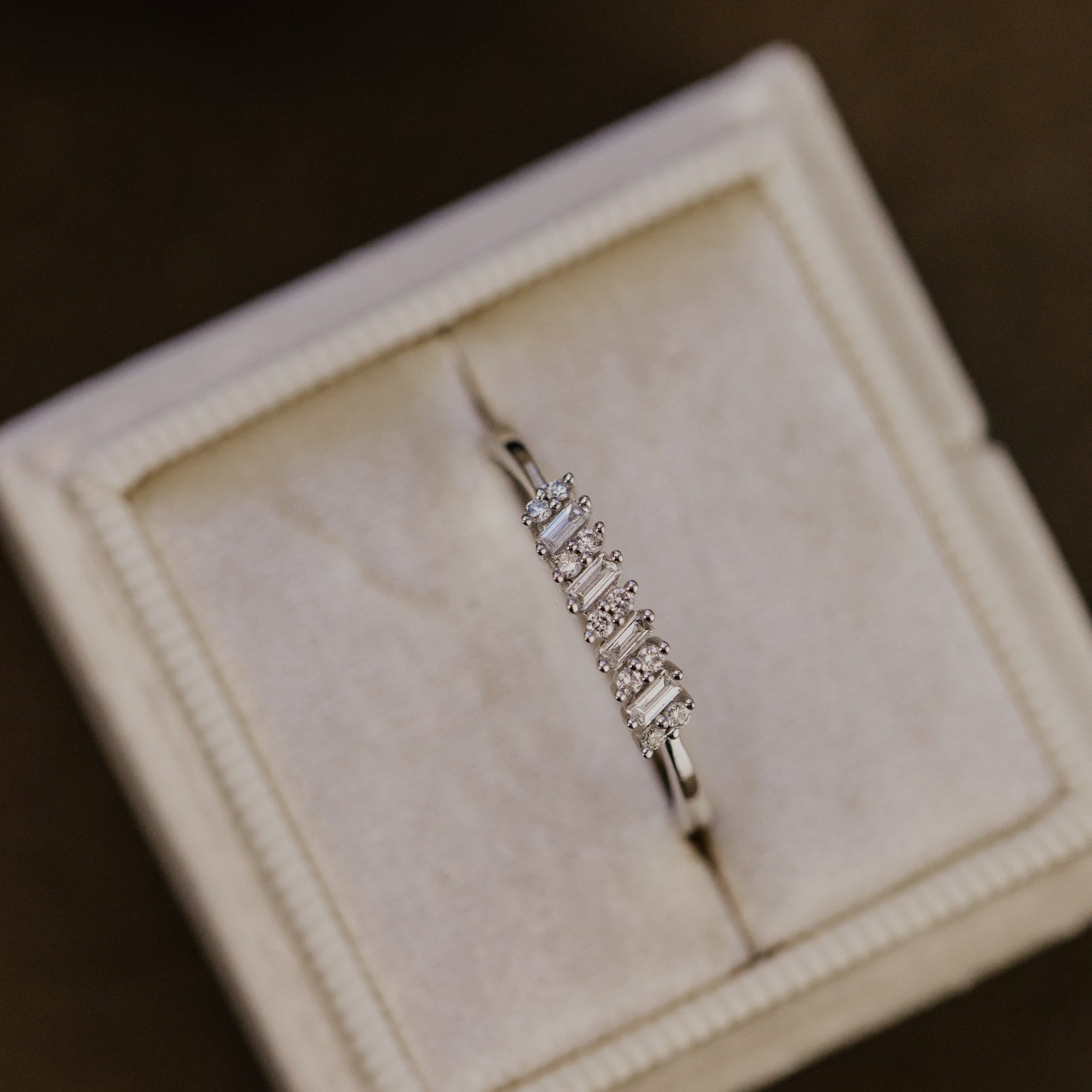 White gold wedding band with diamonds in a jewelry box on a dark surface.
