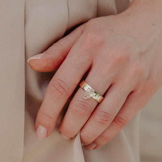 Hand wearing a gold ring with a pear shaped champagne diamond on a beige background