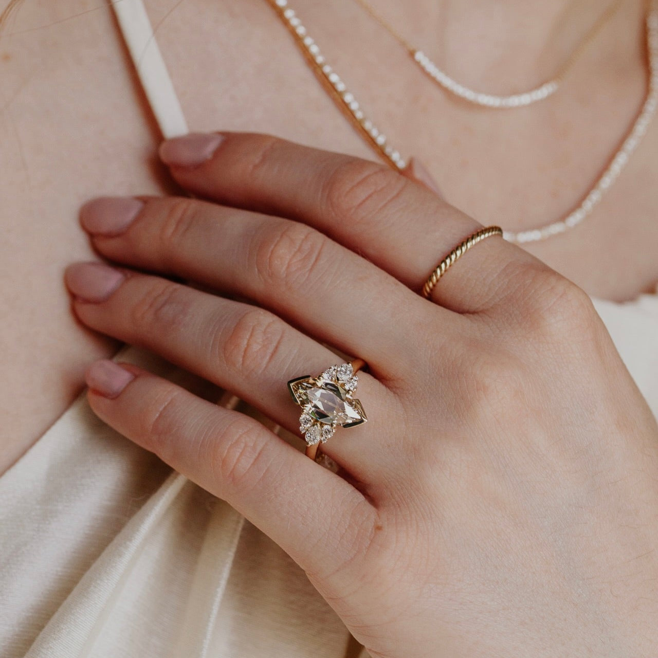 Close-up of a hand wearing a gold ring with a marquise old mine cut light yellow  diamond, set against a neutral background.