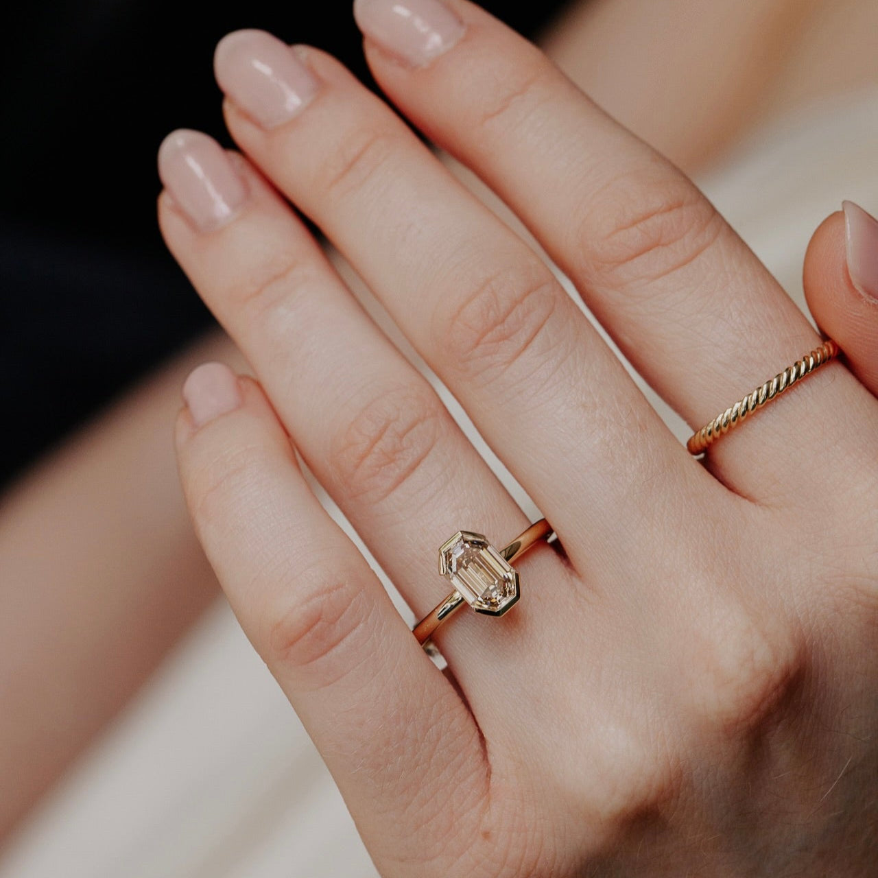 Close-up of a hand wearing a yellow gold ring with a diamond on a blurred background