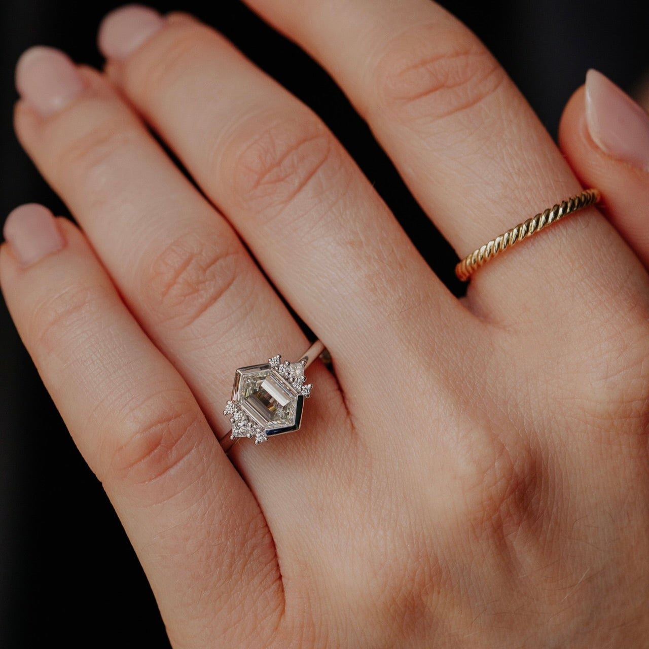 Hand wearing a diamond ring with a dark background