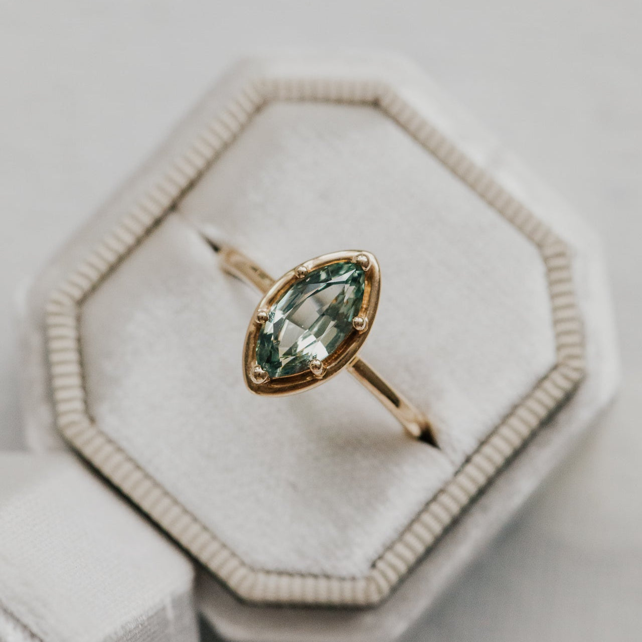 Gold ring with a green sapphire gemstone in a hexagonal box on a light background