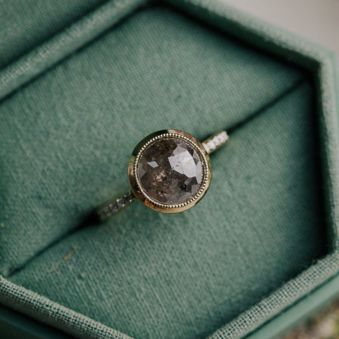 14k gold ring featuring a round grey rustic diamond set in a milgrain bezel with a .09 cttw pave diamond band.