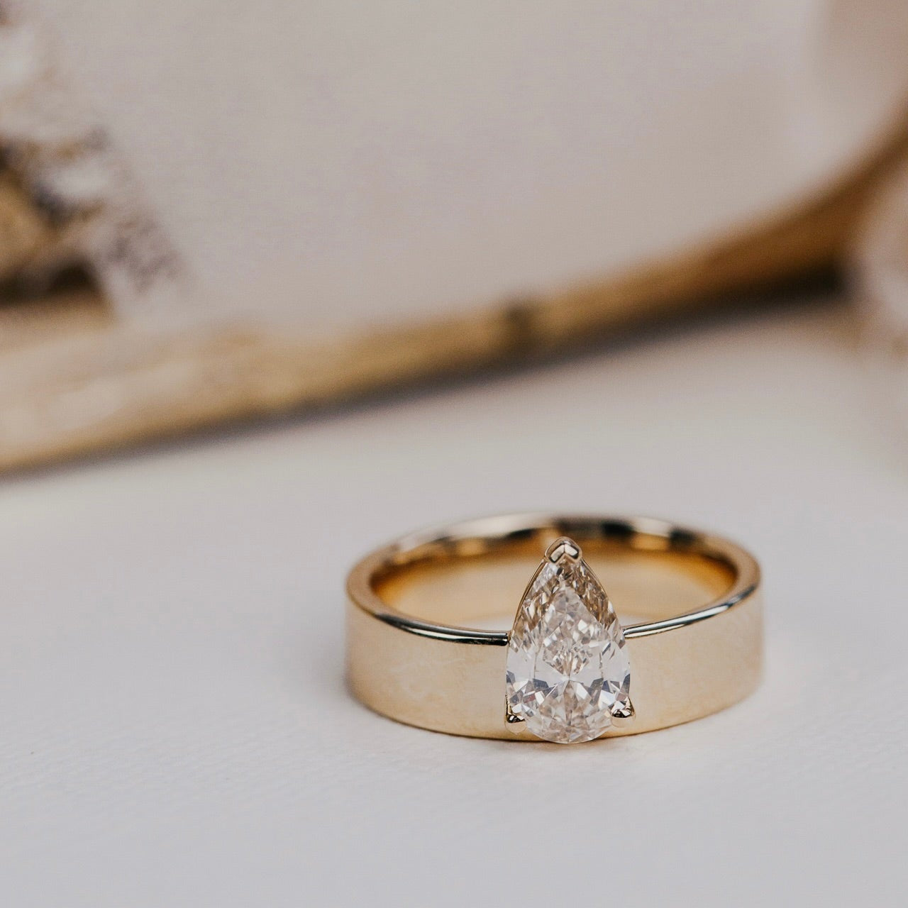 Gold ring with a pear-shaped diamond on a neutral background