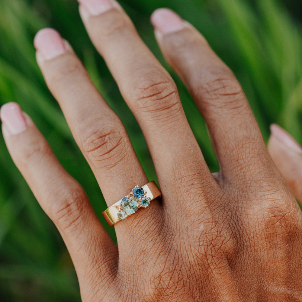 Hand wearing a ring with Australian Sapphire gemstones against a blurred green background