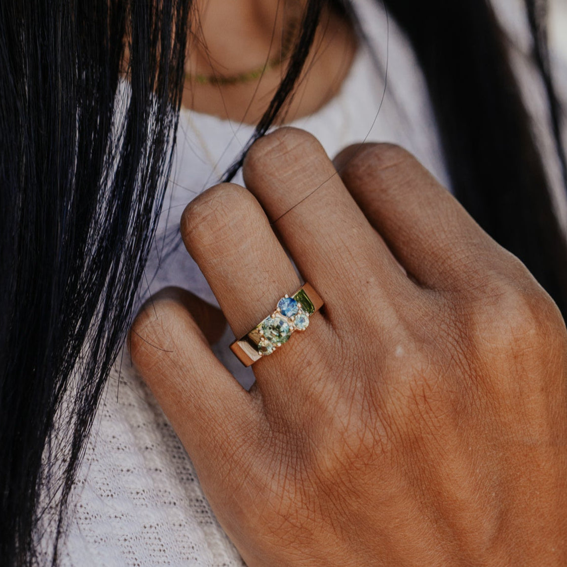 Close-up of a hand wearing a ring with multiple Australian Sapphire gemstones, blurred background