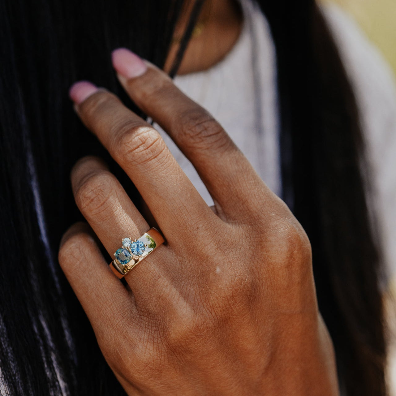 Close-up of a hand wearing a gold ring with a blue sapphires, blurred background