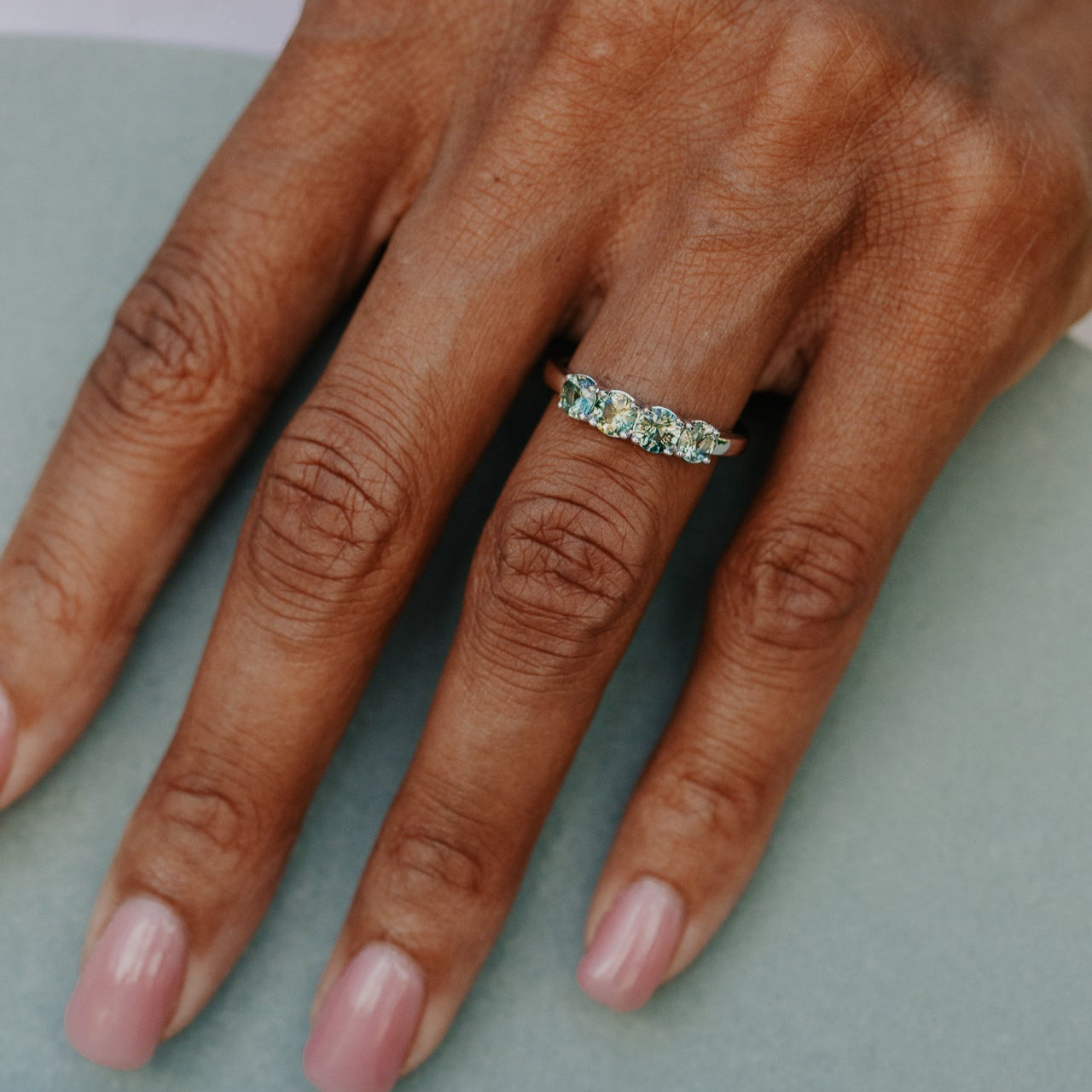 Hand wearing a ring with green and yellow sapphires on a light background