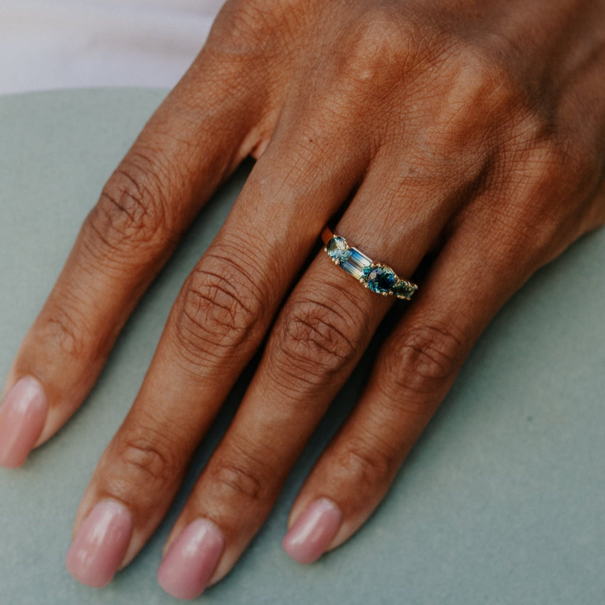 Hand wearing a ring with blue Australian sapphire gemstone on a light background