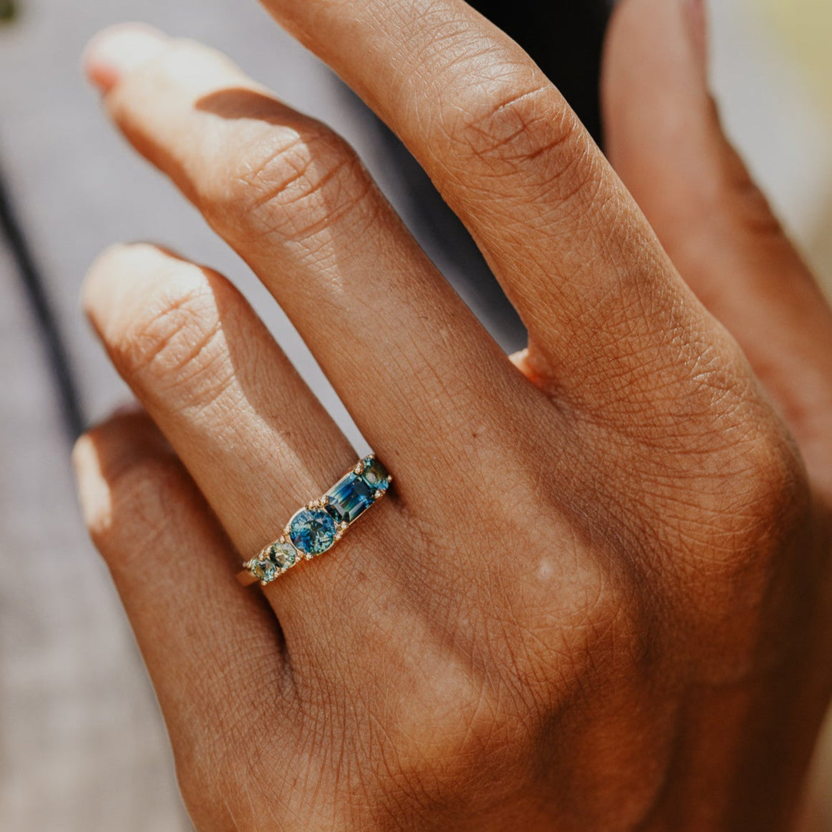 Close-up of a hand wearing a ring with blue Australian sapphire gemstones on a blurred background