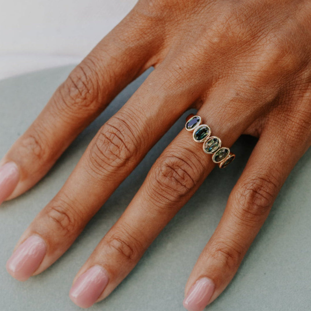 Hand wearing a ring with green Australian Sapphiresgemstones on a light background