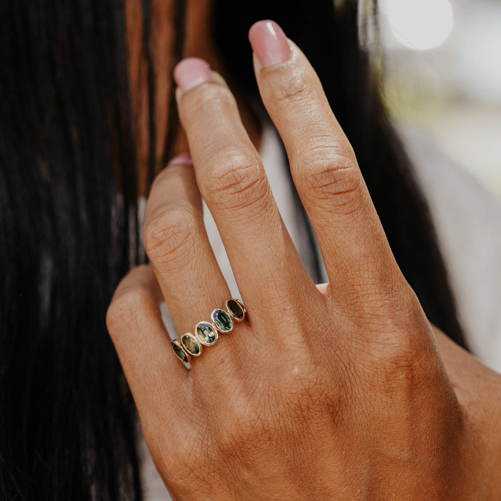 Hand wearing a ring with three Australian Sapphires green gemstones against a blurred background