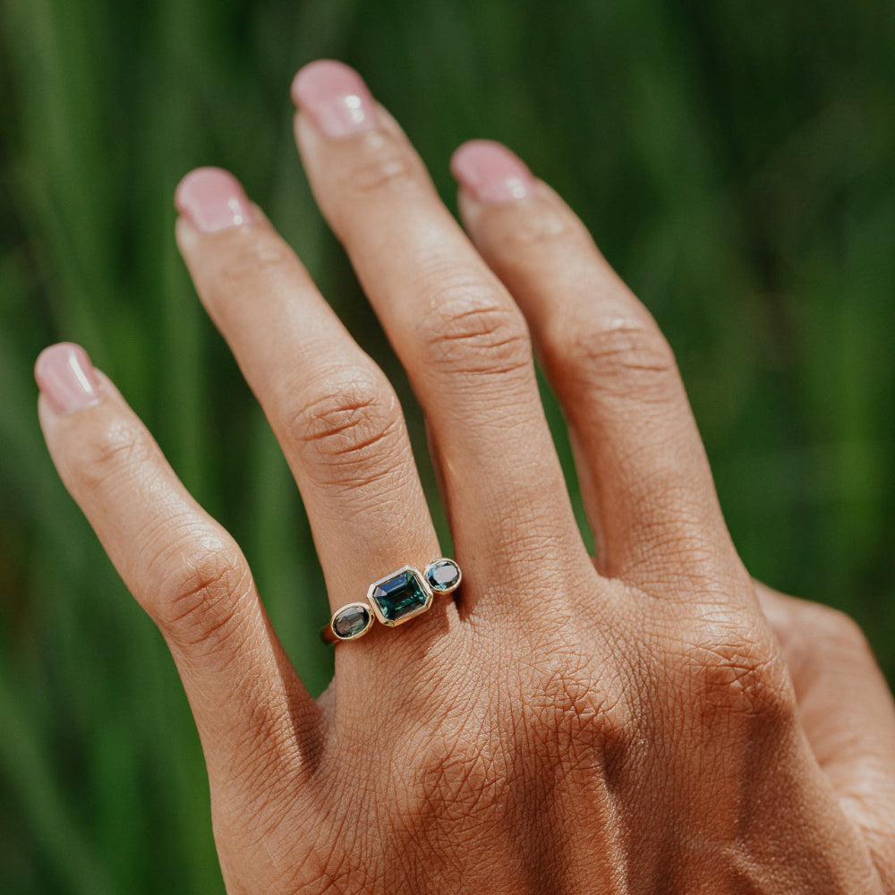Hand wearing a ring with green Australian sapphire gemstones against a blurred green background