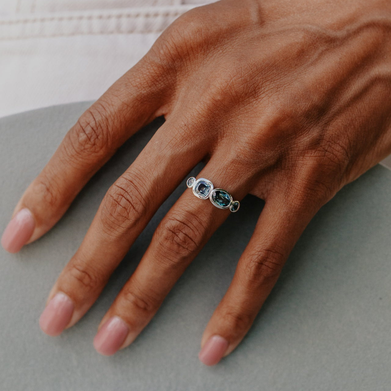 Hand wearing a white gold ring with multiple blue sapphires on a neutral background