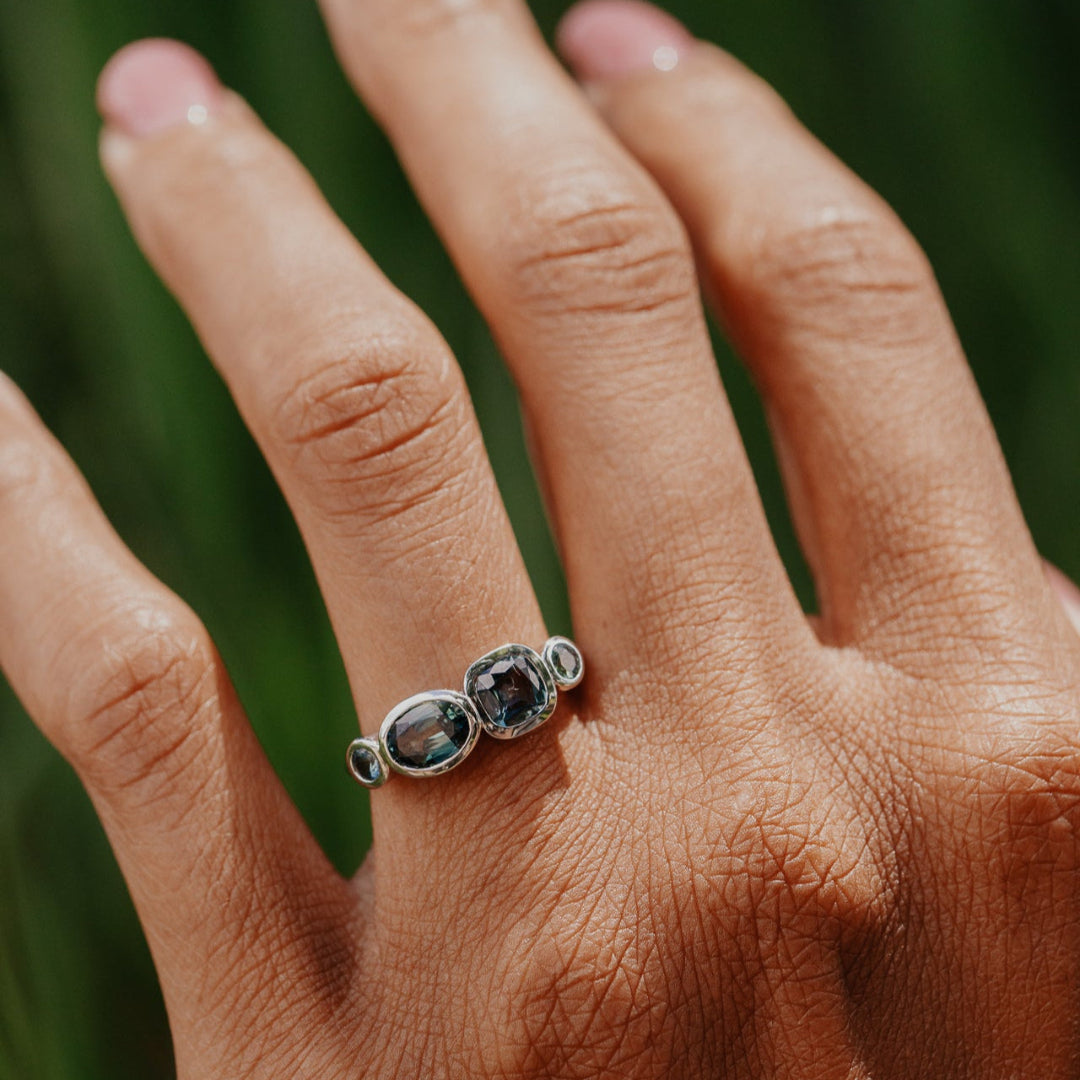 Hand wearing a white gold ring with multiple sapphires against a blurred green background