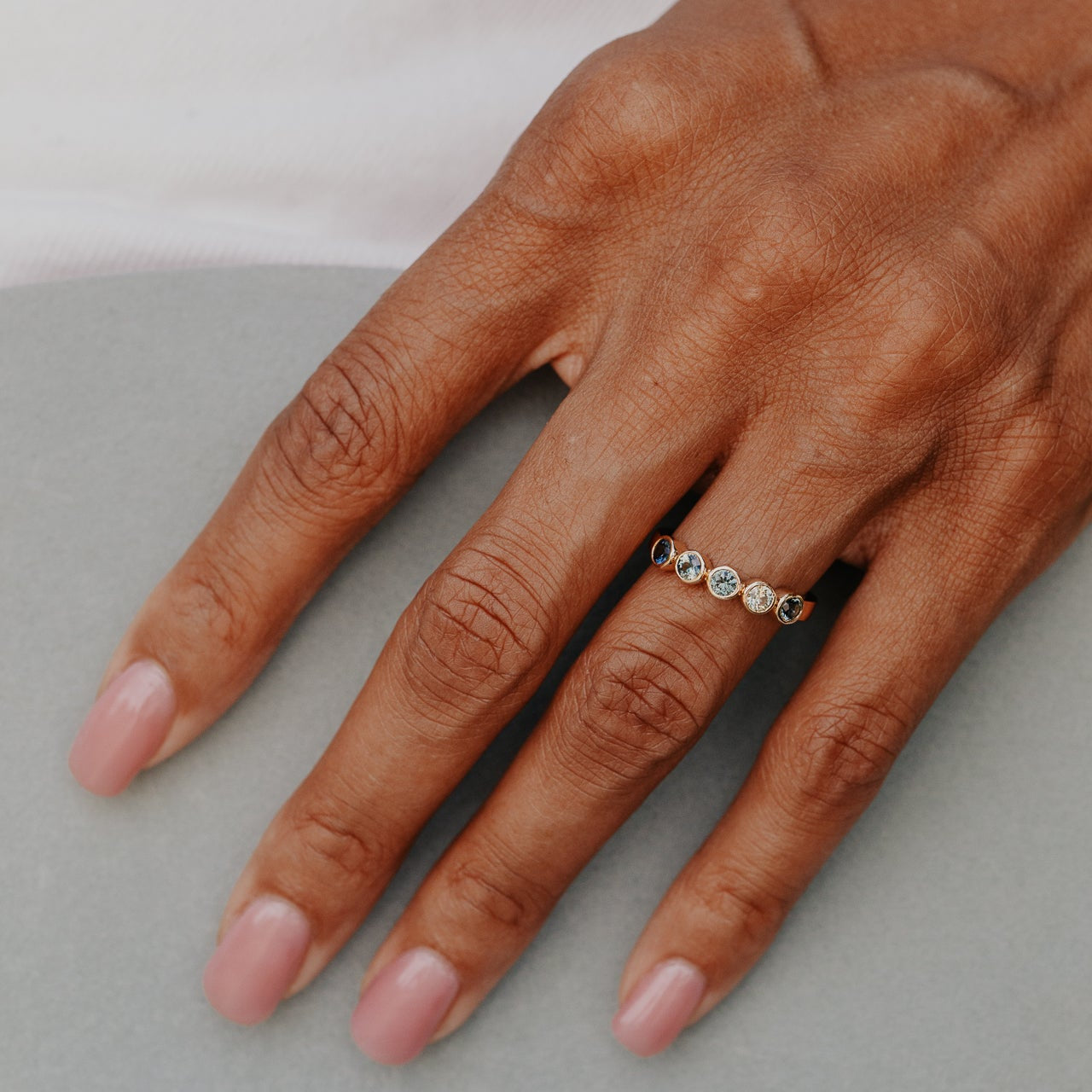 Hand wearing a ring with multi-colored sapphires on a neutral background