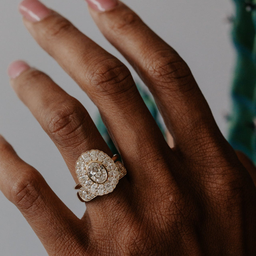 Close-up of a hand wearing a oval diamond halo ring with a blurred background