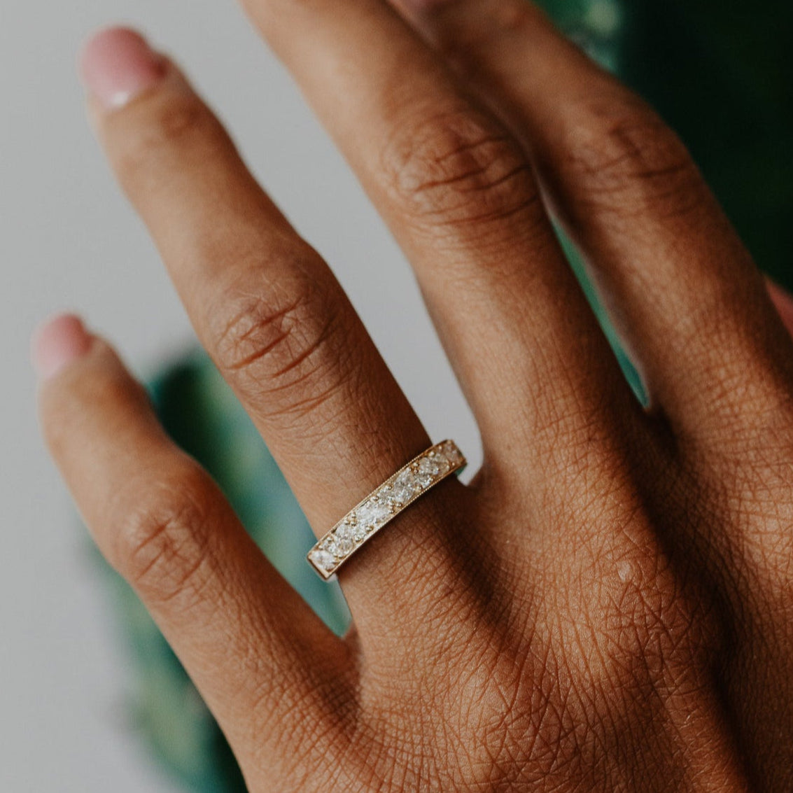 Hand wearing a diamond ring with a blurred green plant background