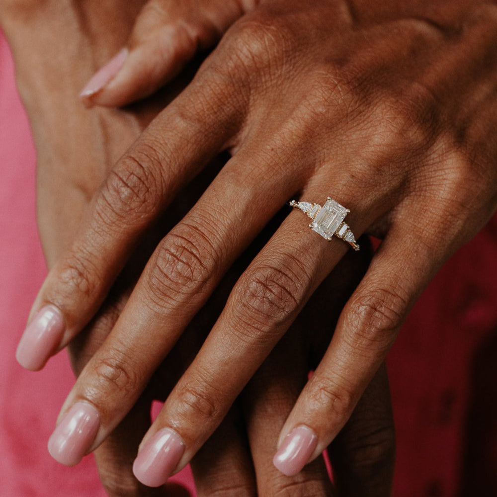 Close-up of a hand wearing a diamond  emerald cut ring with a pink background