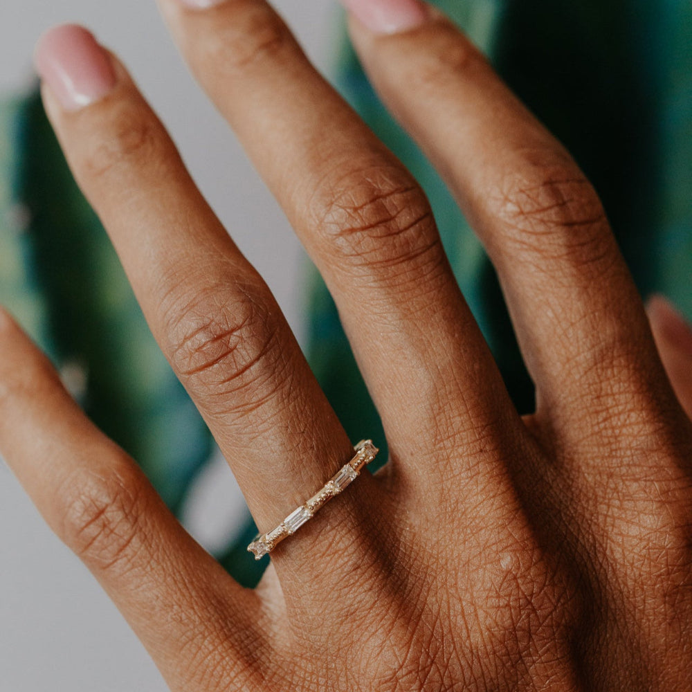 Close-up of a hand wearing a gold diamond band with a blurred background