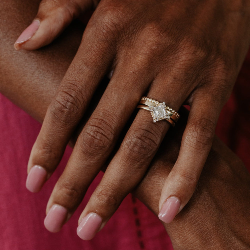 Close-up of a hand wearing a diamond ring with a gold band on a  blurred red background