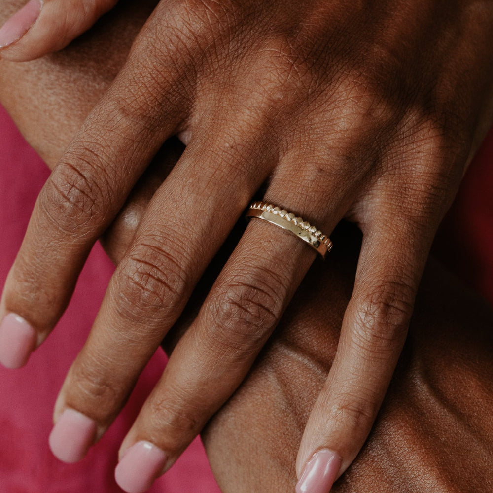 Close-up of a hand wearing a gold band with a pink background