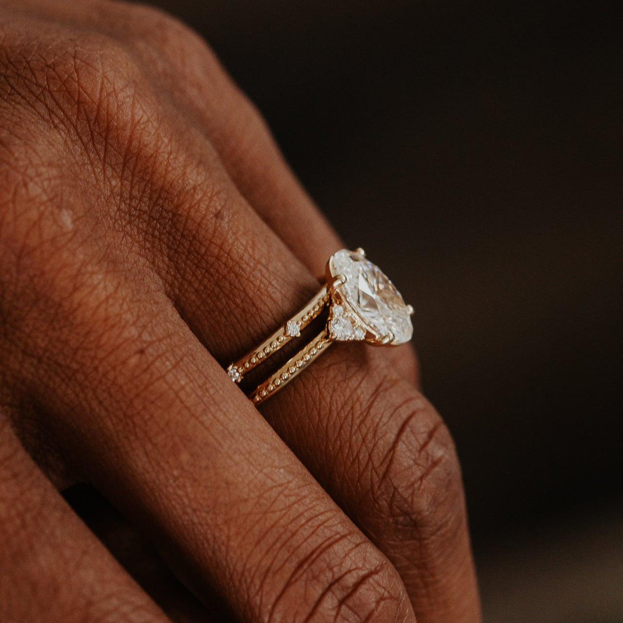 Gold band with a diamond on a person's finger against a dark background