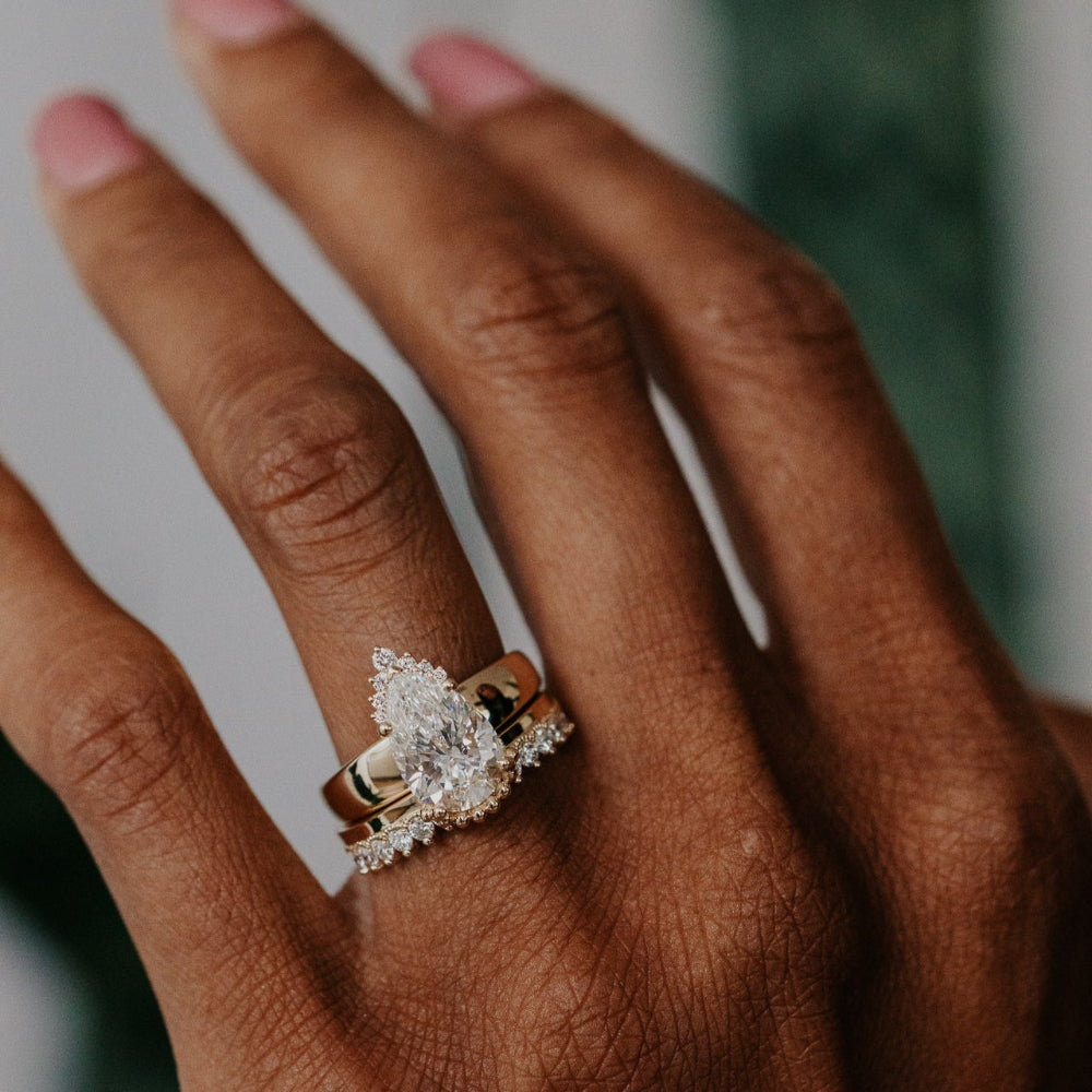 Close-up of a hand wearing a pear shaped diamond ring with a blurred background