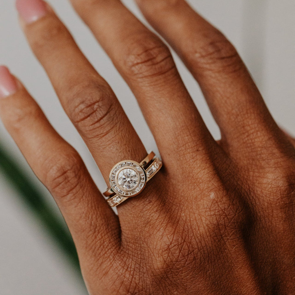 Yellow gold ring with a round diamond halo on a hand against a neutral background