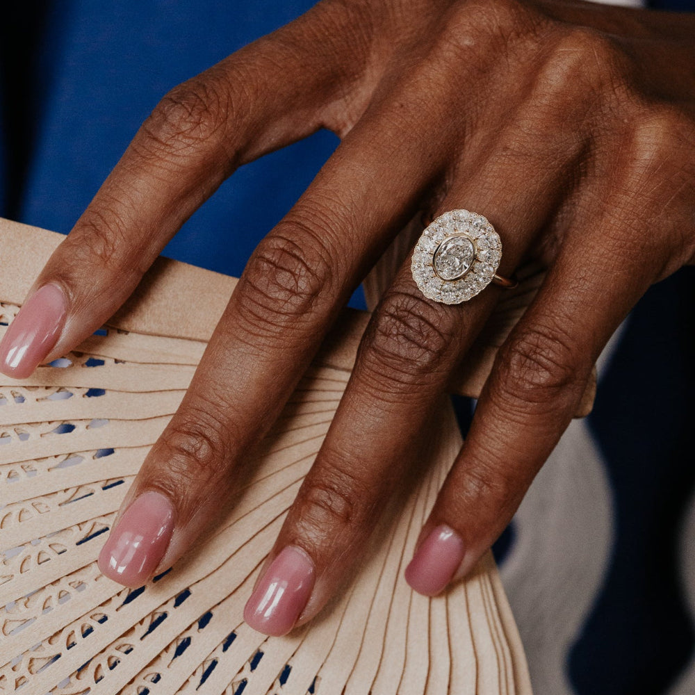 Hand with a oval diamond double halo ring holding a fan against a blue and white striped background