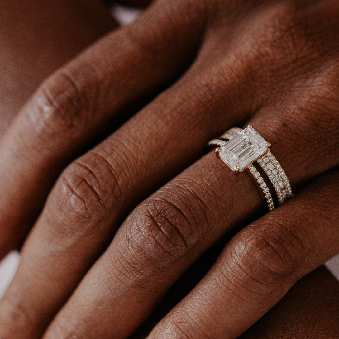 14k gold wedding band with alternating horizontal baguette and round diamonds set between two rows of round pave diamonds paired with a emerald cut diamond solitaire ring