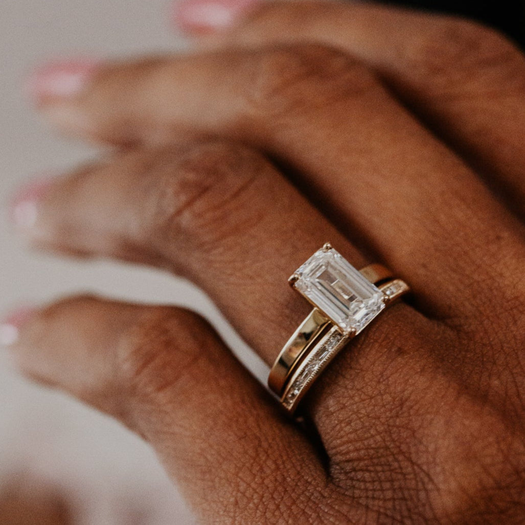 14k gold band featuring ~ .22 cttw baguette and round diamonds set in milgrain detail edges paired with a emerald cut diamond solitaire ring