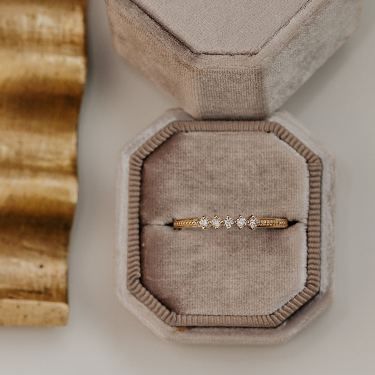 round diamond set in prongs on a flat 14k gold wedding band with a milgrain texture