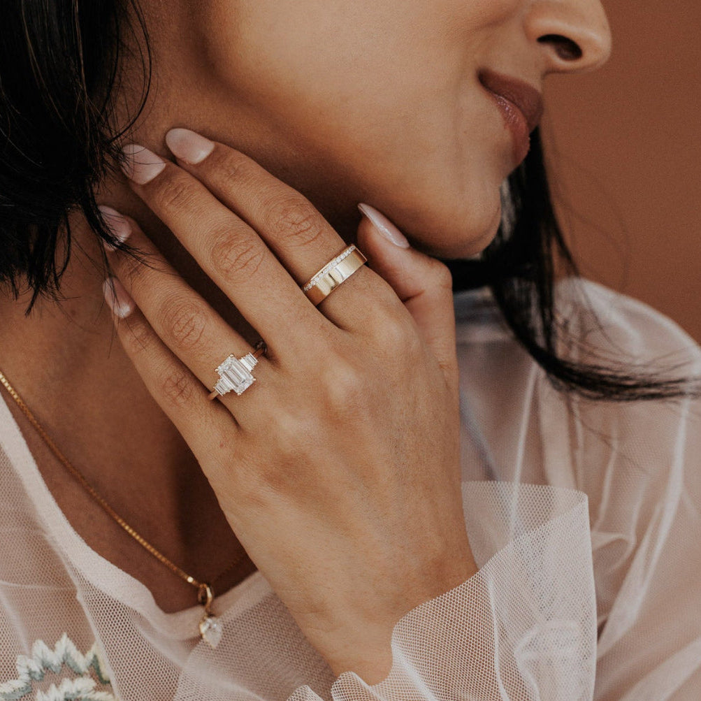 The Jolee Emerald Cut Ring in 14k yellow gold worn on the ring finger, styled with a wide gold band on the middle finger.