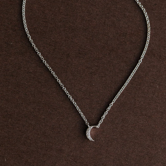 White gold necklace with a crescent moon pendant on a brown background