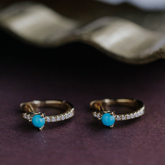 Pair of gold rings with turquoise stones on a dark surface