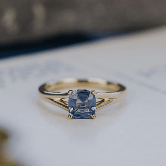 A 14k gold ring featuring a blue Montana sapphire gemstone, displayed on a white surface with a soft background. 