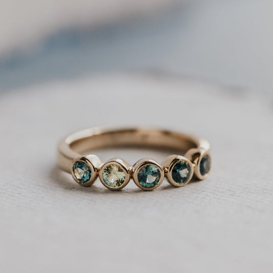 Gold ring with embedded multi-colored sapphires on a light background